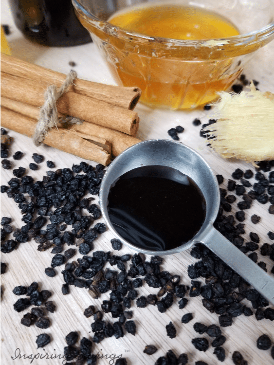 Homemade elderberry syrup in tablespoon next to loose elderberries