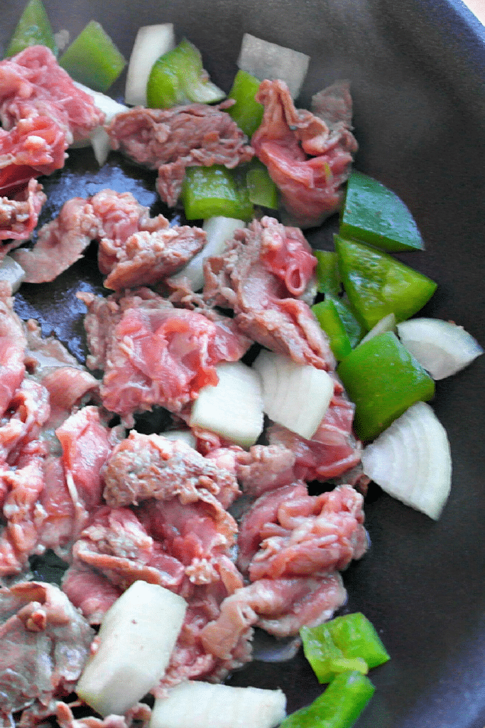 Steak and onions cooking in saute pan on stove - medium heat