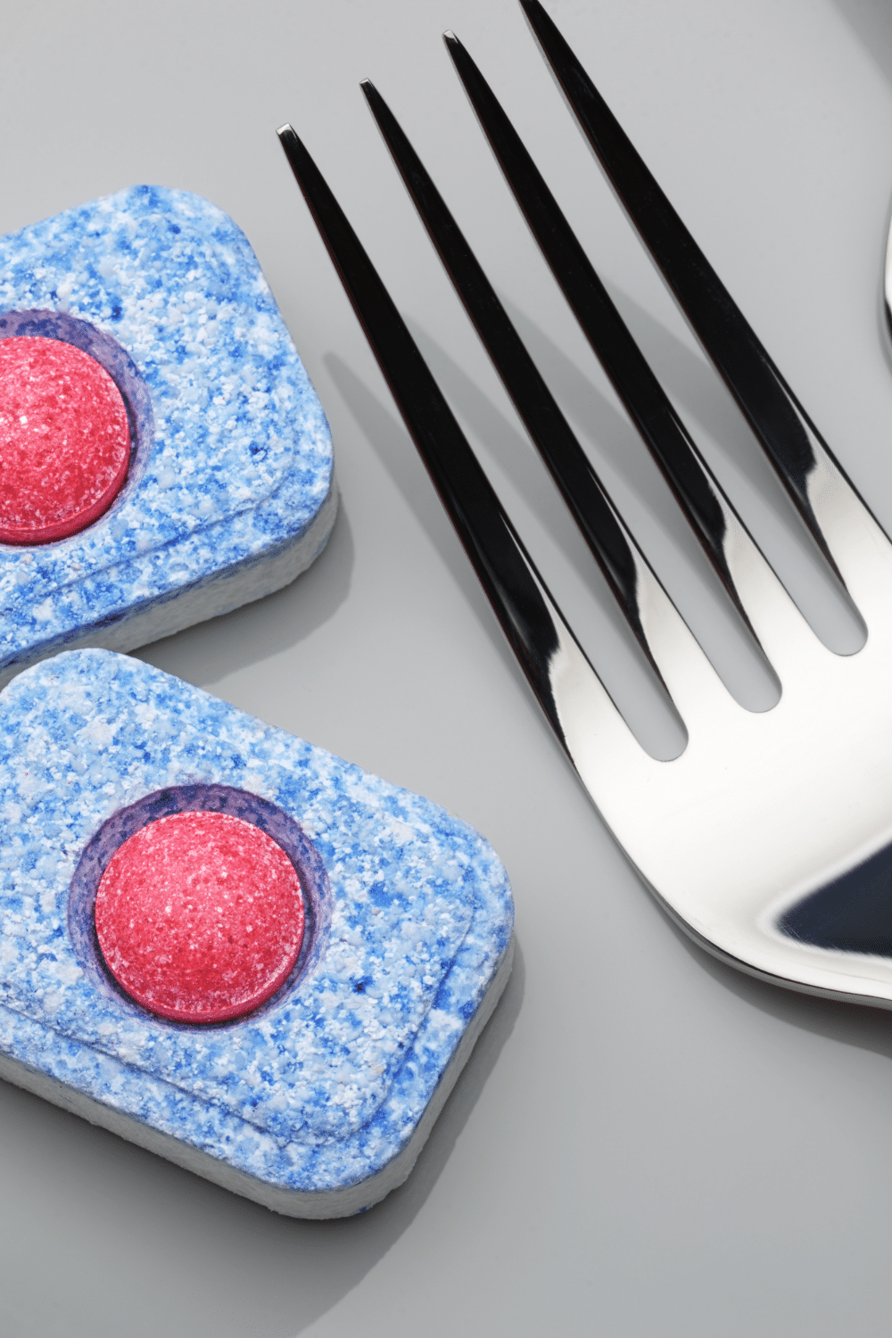 two dishwasher tablets and clean fork on grey background